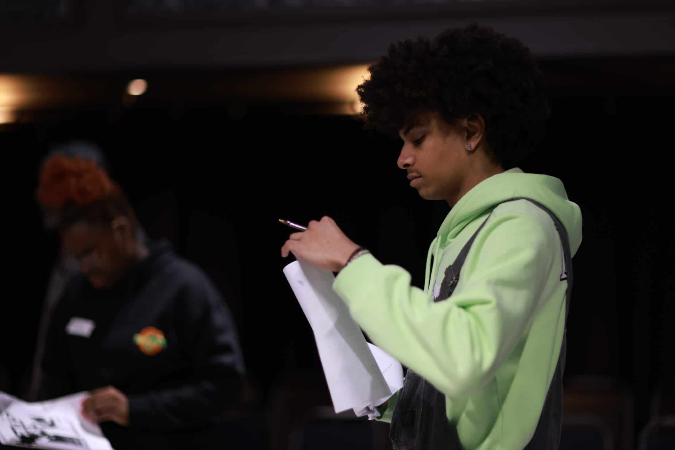 Institute for Contemporary Theatre student with green hoodie holding a script with another student in the background