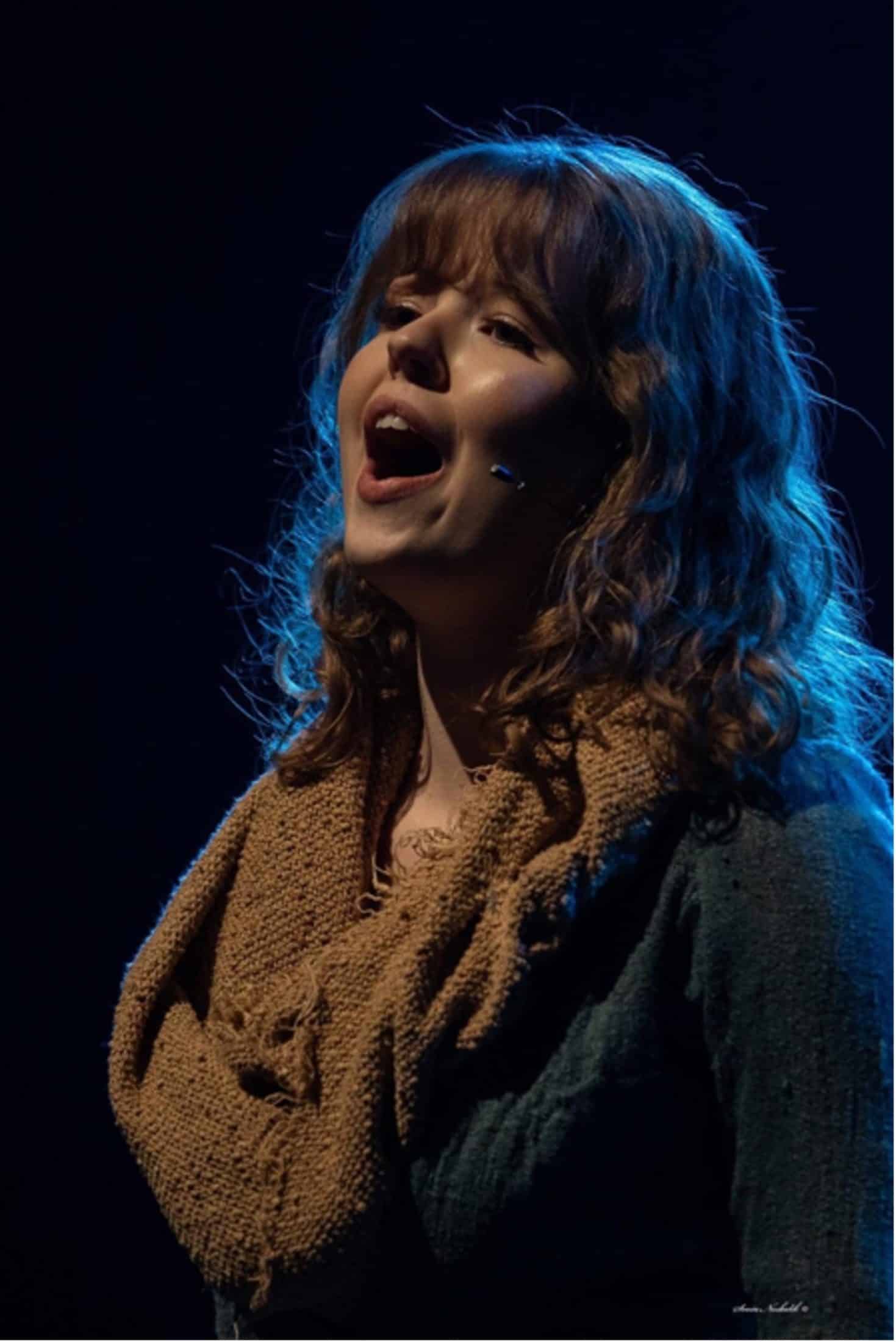 Portrait of Eline Jacobsen singing with black background and blue lighting on her hair 